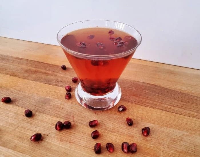 Martini glass filled with red liquid and garnished with pomegranate arils.