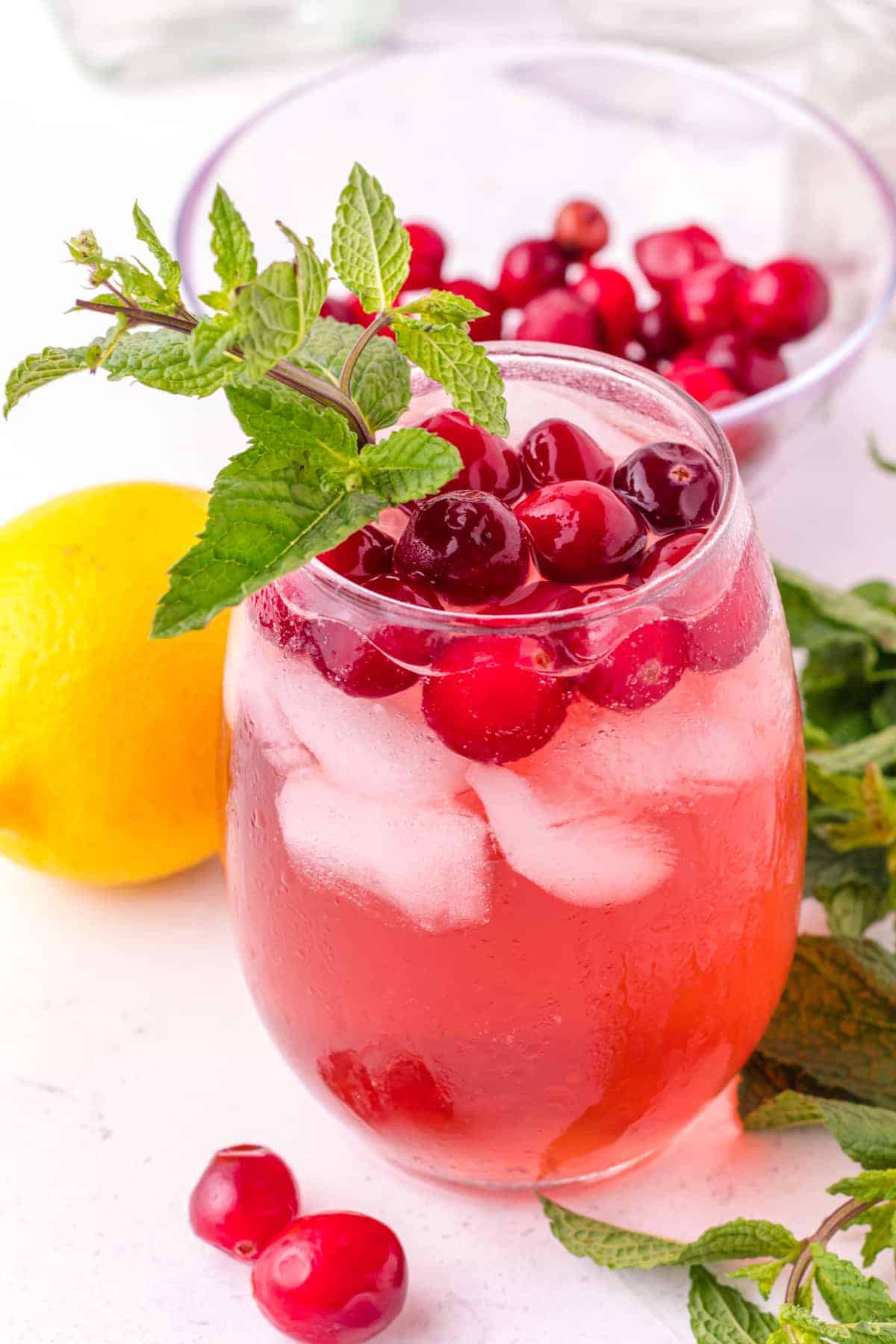 Stemless wine glass with a red cocktail, garnished with mint and cranberries.