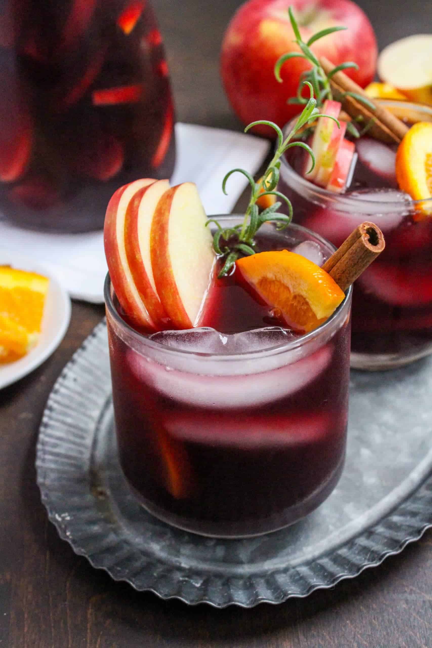 Glasses filled with dark red sangria, with rosemary, apple slices, orange slice and cinnamon as garnish.