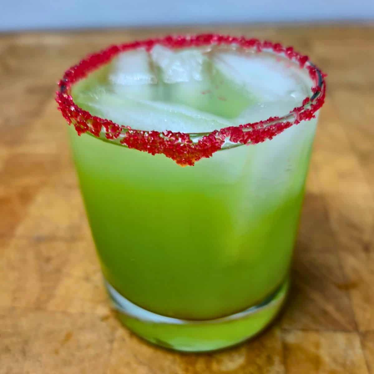 Green cocktail in an old fashioned glass, with a red sugar rim.