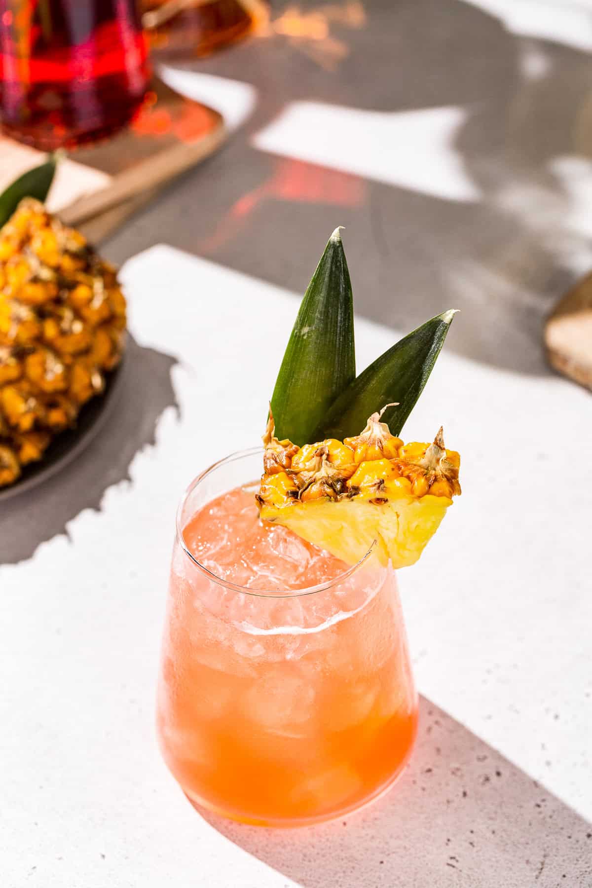 Jungle Bird cocktail with pineapple garnish on a countertop. In the background is a bottle of Campari and fresh pineapple.