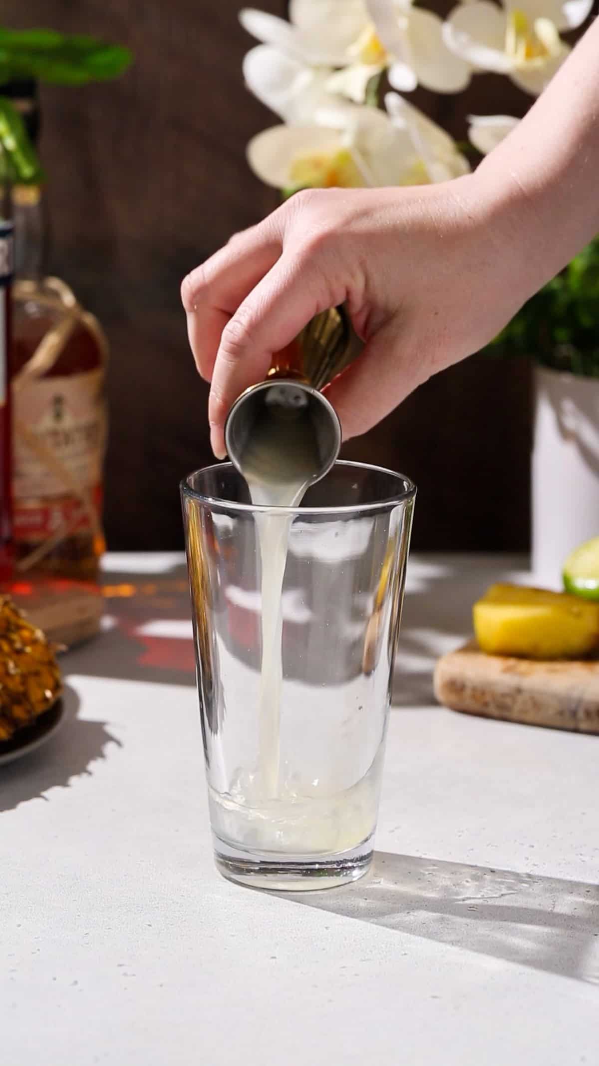 Hand adding lime juice to a cocktail shaker.