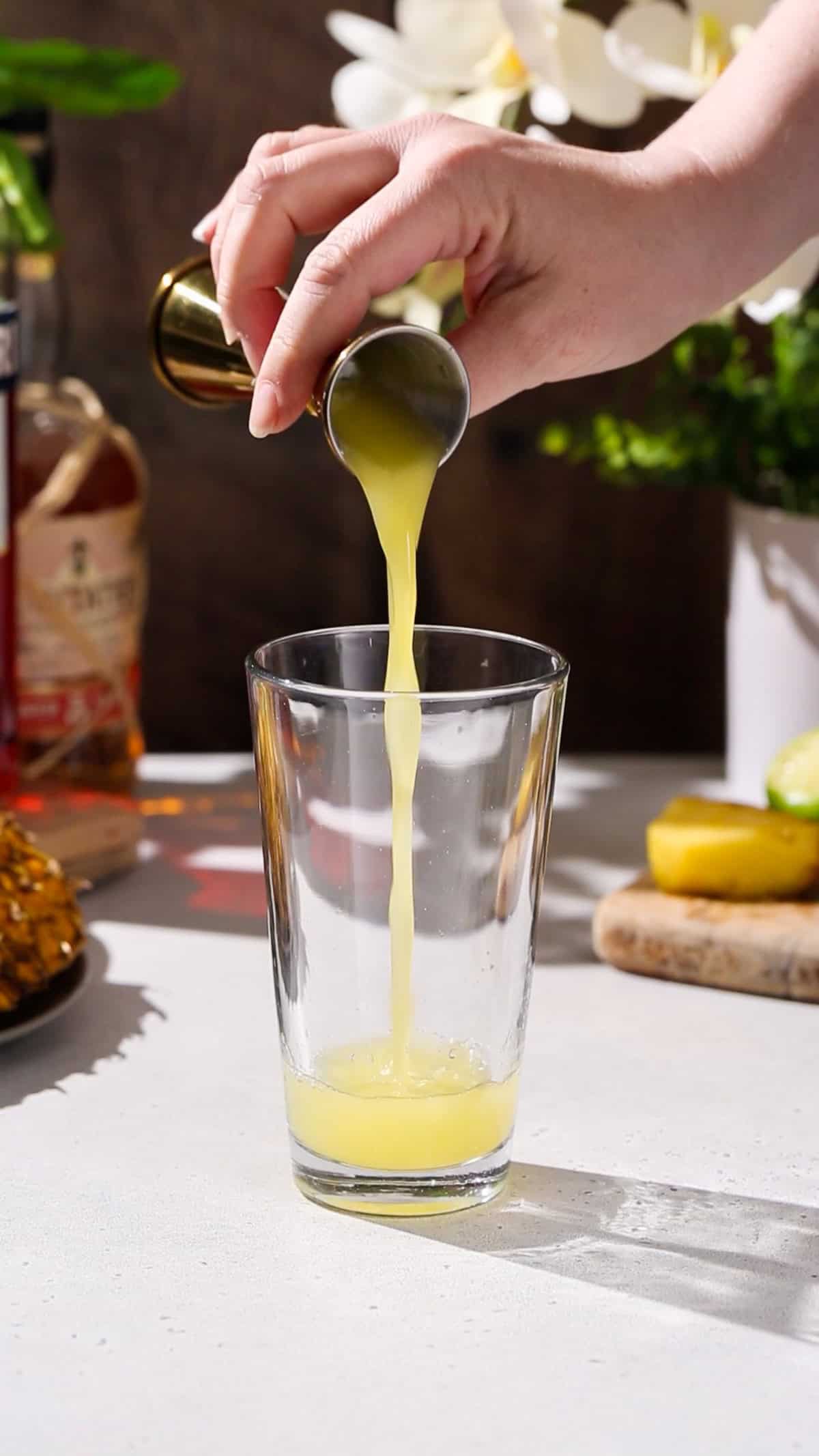 Hand adding pineapple juice to a cocktail shaker.