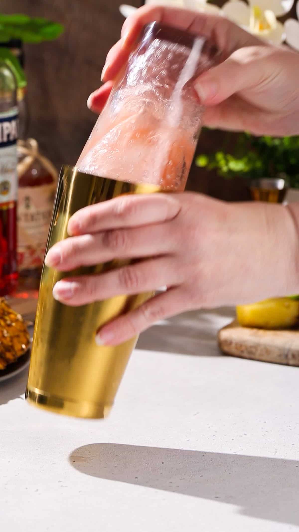 Hand using a cocktail shaker to shake up an orange colored cocktail.