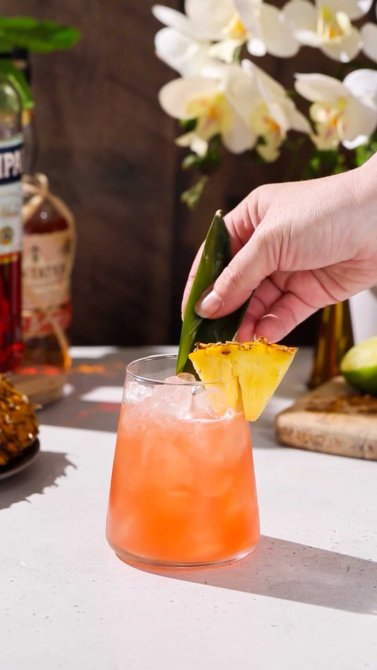 Hand adding pineapple fronds to garnish a tropical looking cocktail.