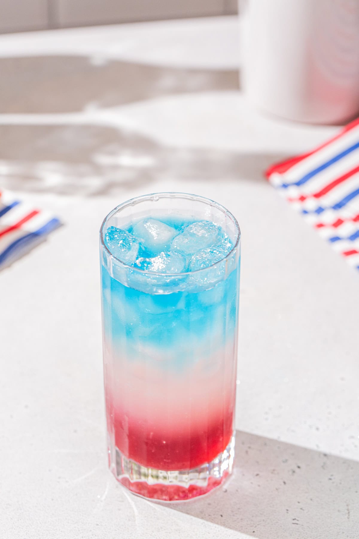 Red, white and blue cocktail on a countertop with striped colored napkins in the background.