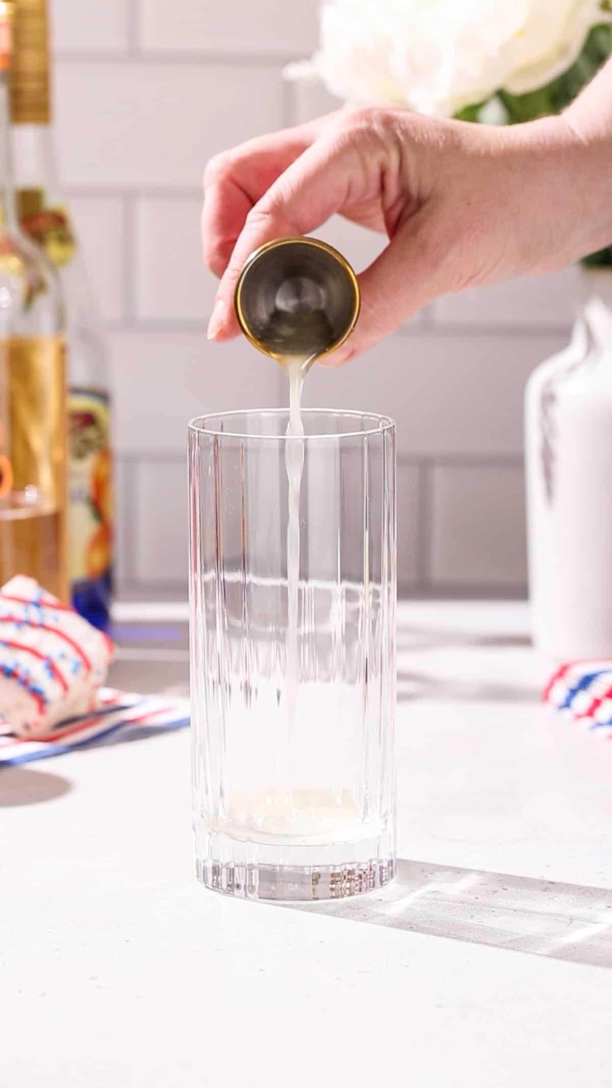 Hand pouring lemon juice into a collins glass.