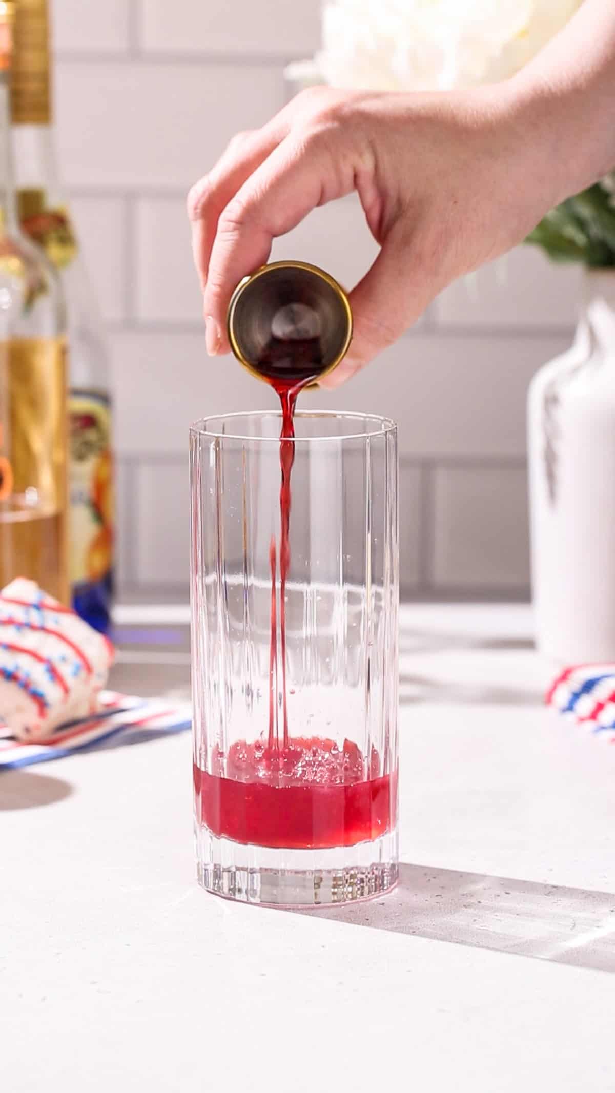 Hand pouring pomegranate juice into a collins glass.