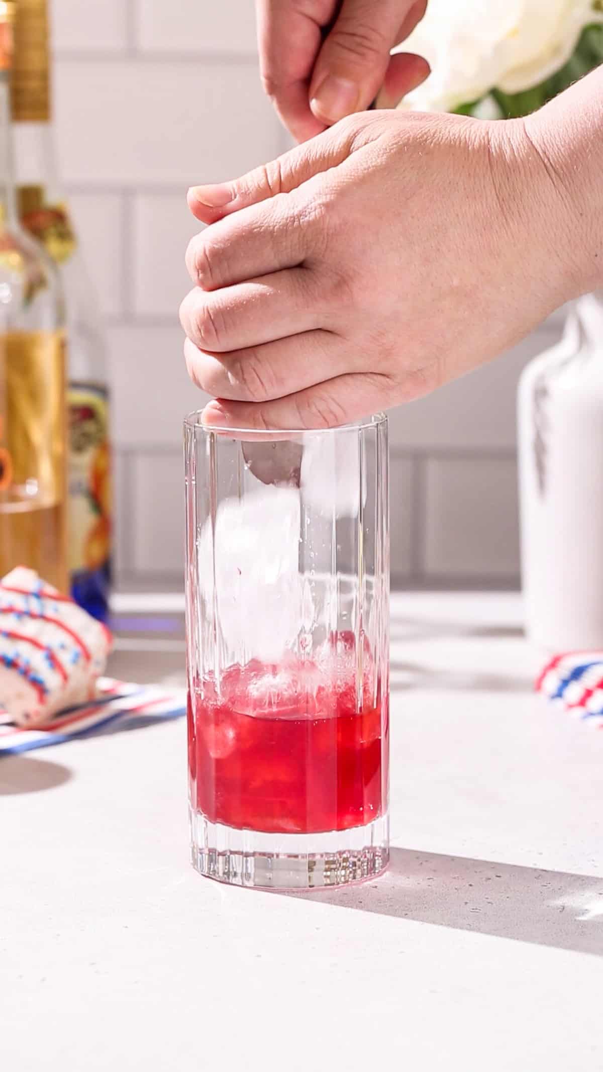 Hand adding ice to a Collins glass.