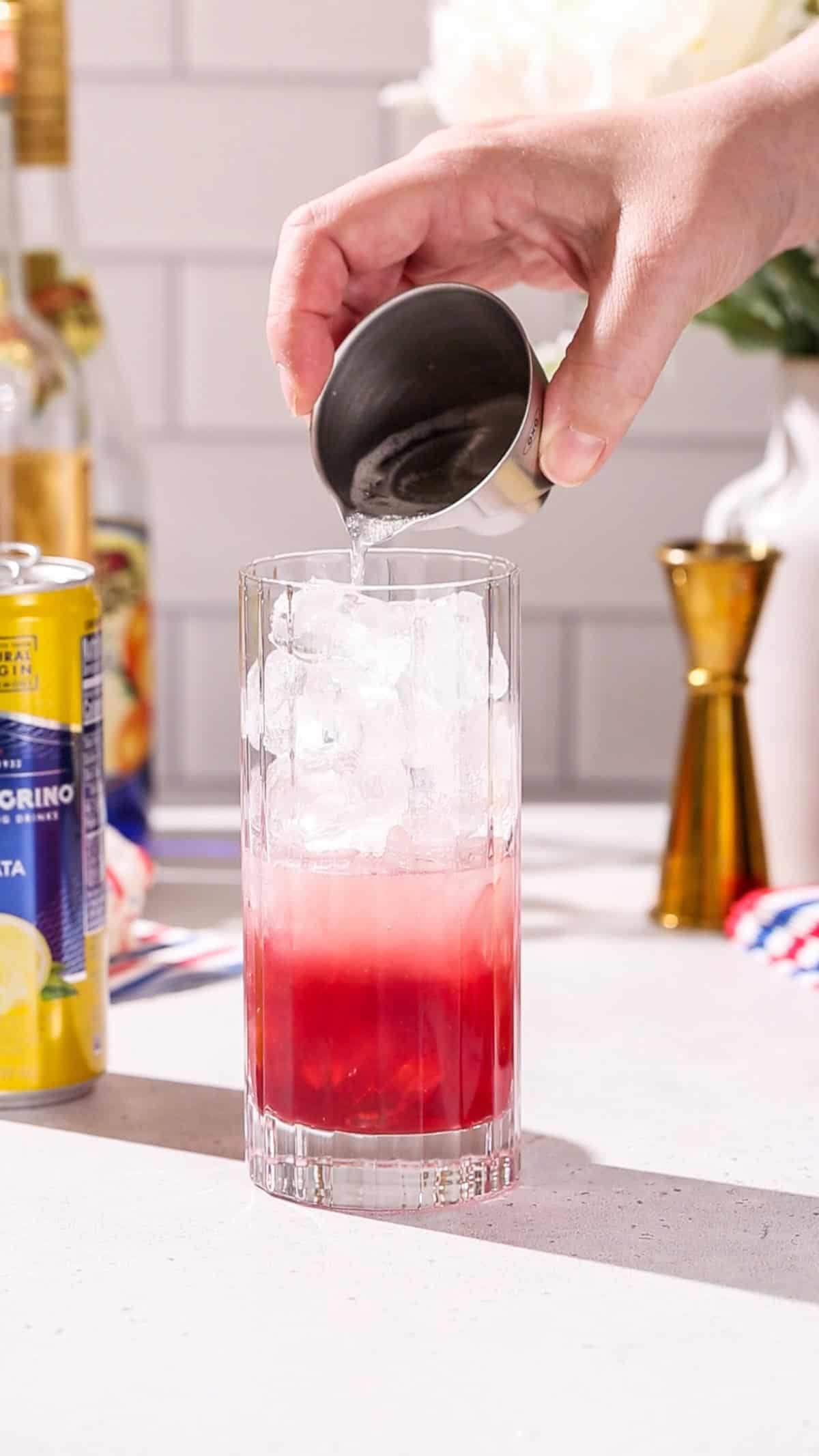 Hand pouring sparkling lemonade into a cocktail glass.