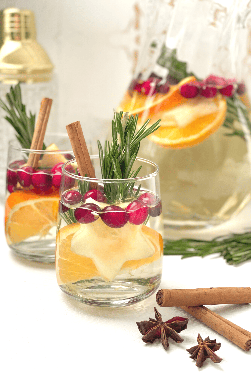 Two glasses of white sangria garnished with star anise, star fruit, cranberries, cinnamon, orange and rosemary.