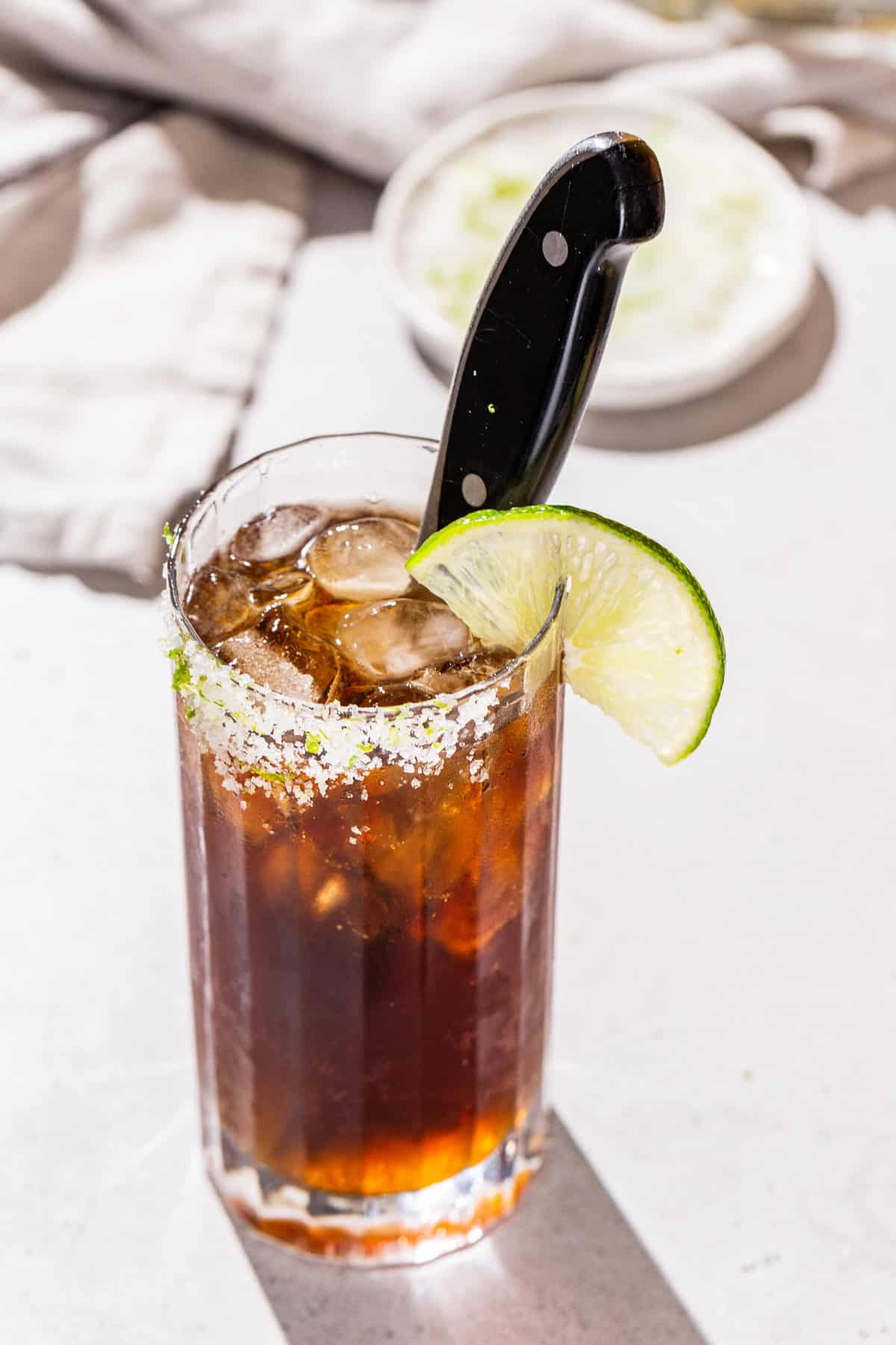 Overhead view of a Batanga cocktail with a lime salt rim and a lime slice as garnish. A knife is in the cocktail as a garnish as well.