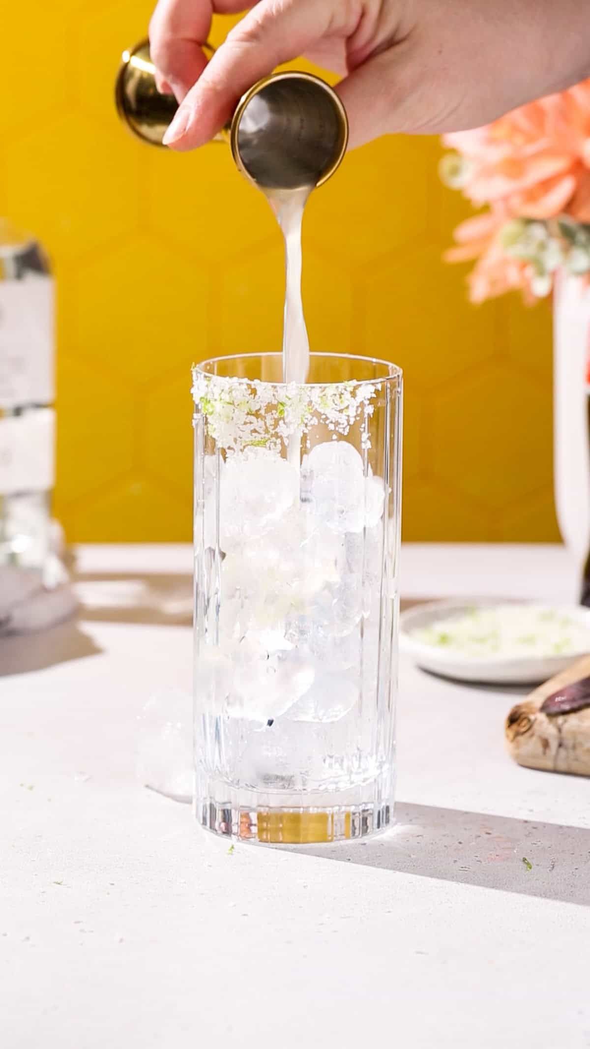 Hand adding lime juice to a cocktail glass filled with ice.