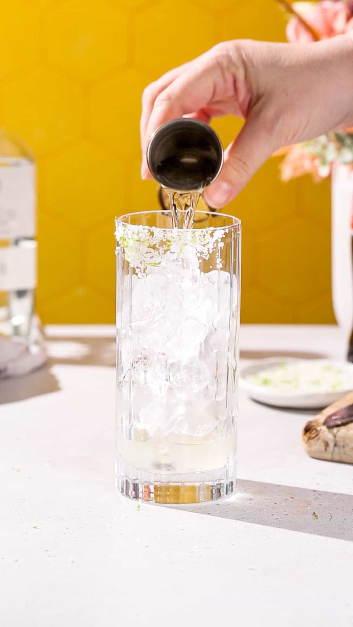 Hand adding tequila to a cocktail glass filled with ice.