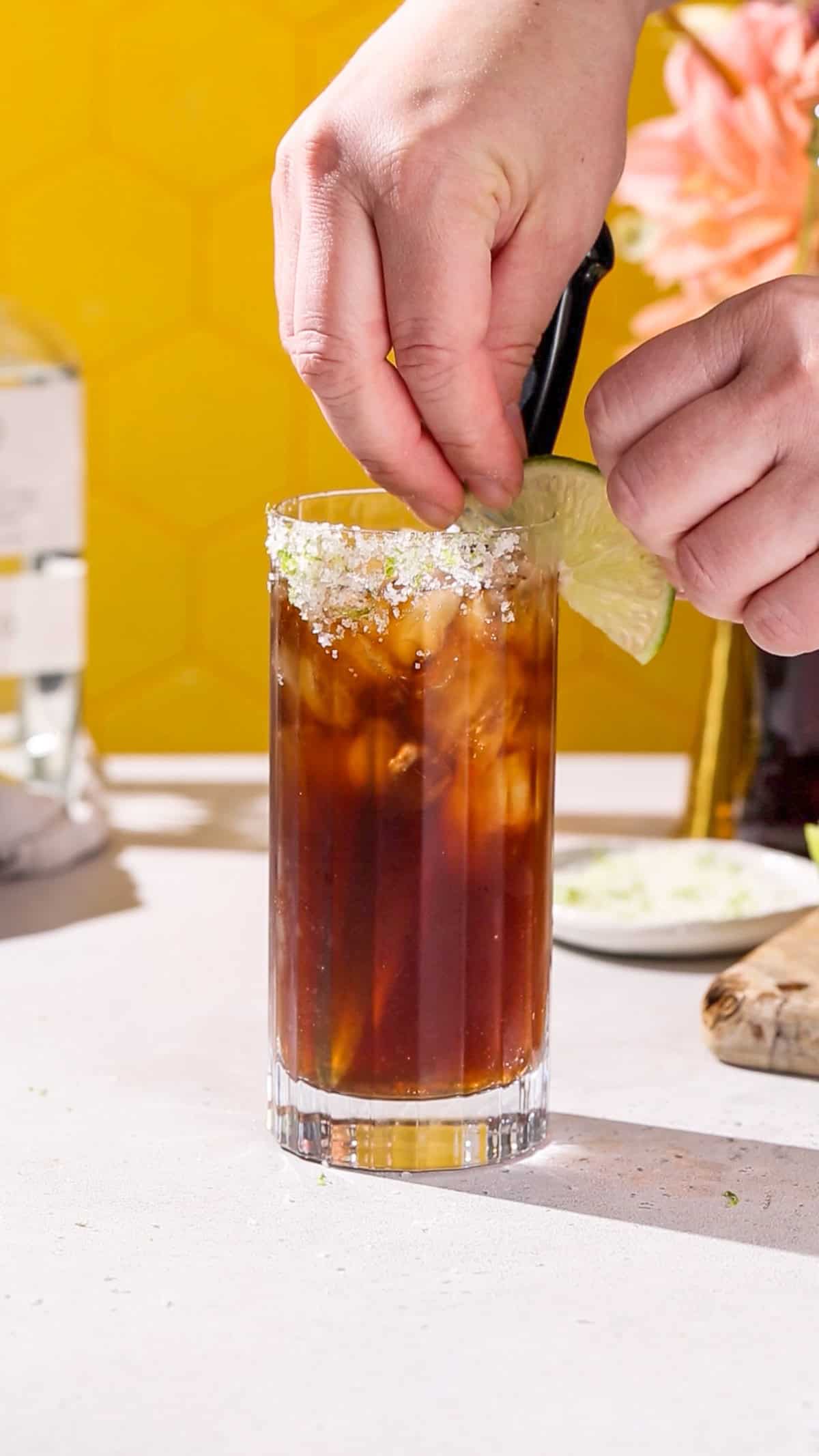 Hand adding a lime garnish to a cocktail.