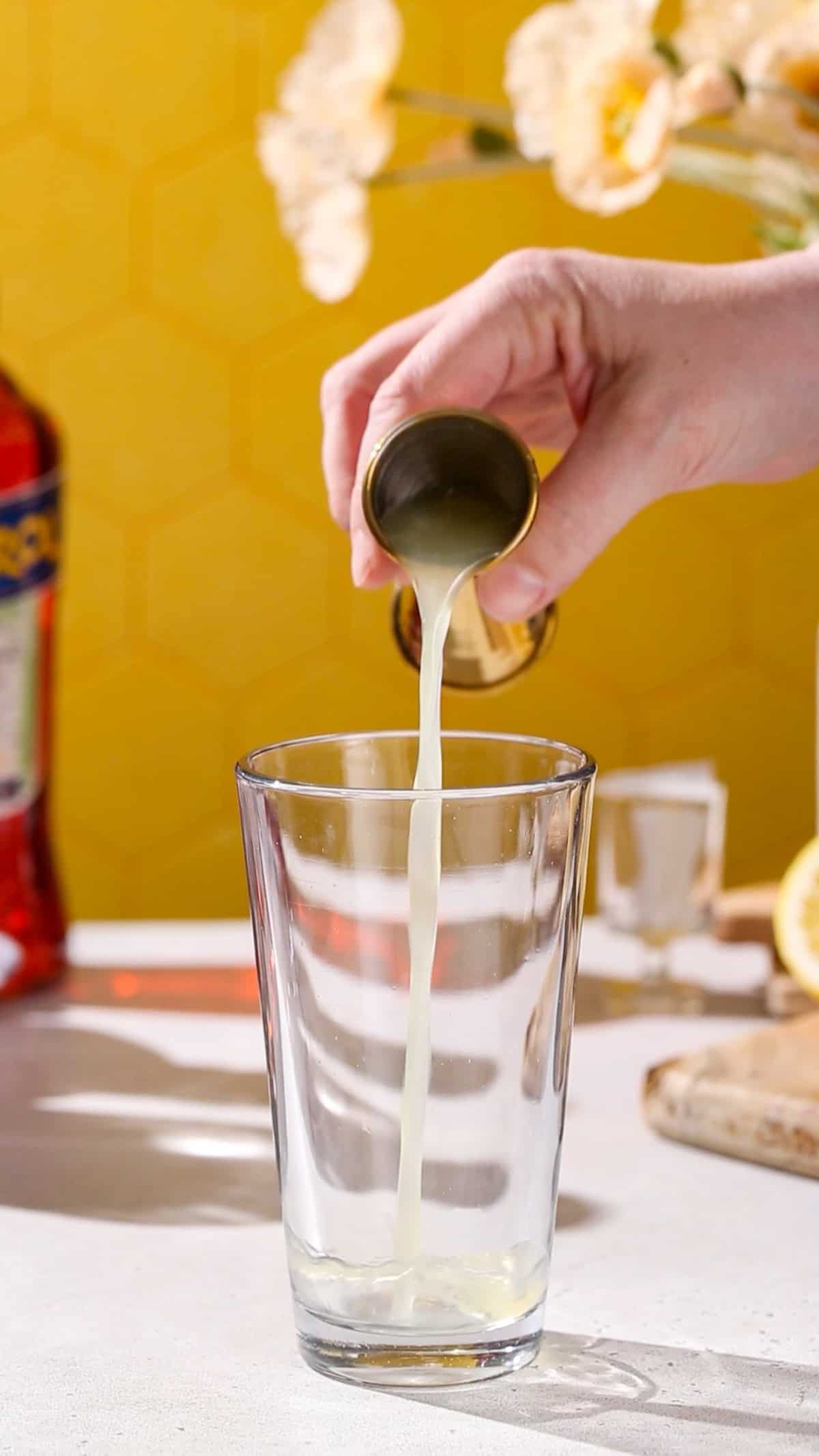 Hand using a jigger to add lemon juice to a cocktail shaker.