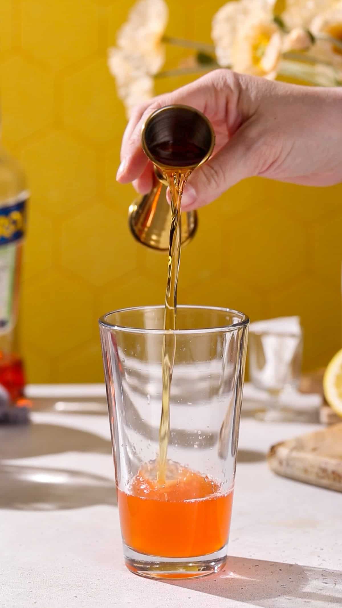 Hand adding bourbon to a cocktail shaker.