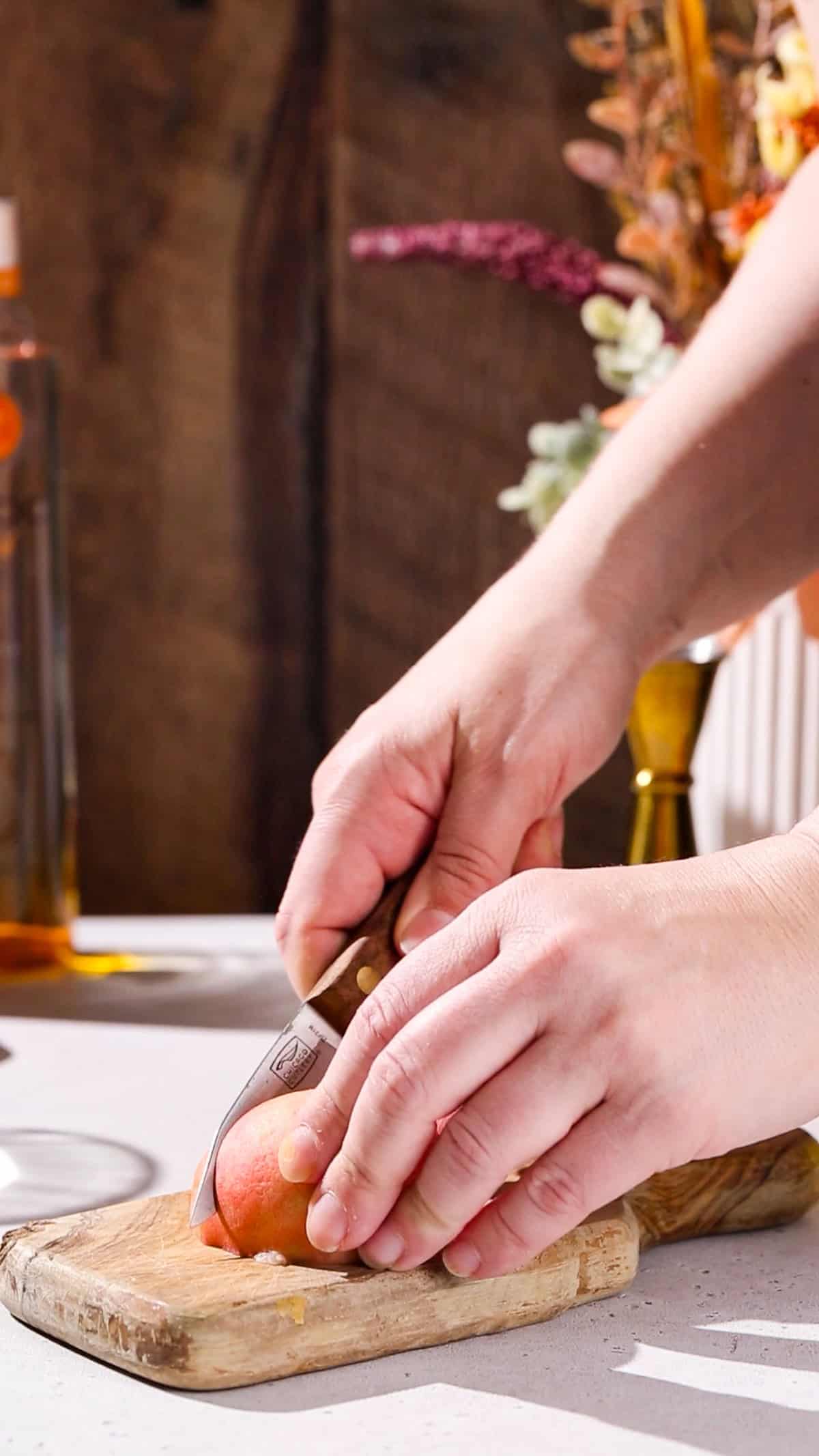 Hands using a paring knife to cut a slice of fresh peach.