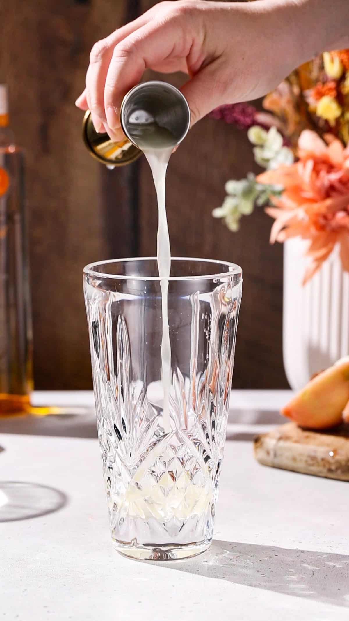 Hand using a jigger to add lemon juice to a cocktail shaker.