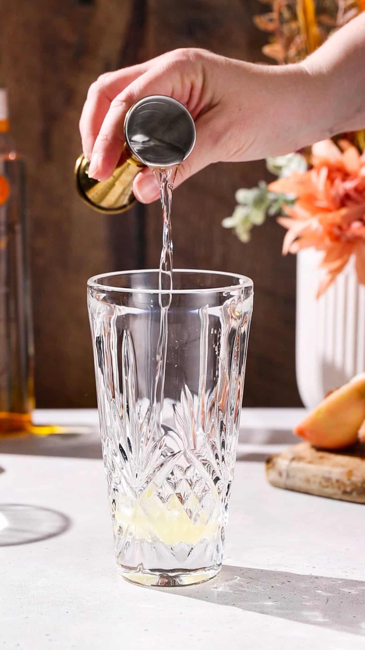 Hand using a jigger to add dry vermouth to a cocktail shaker.