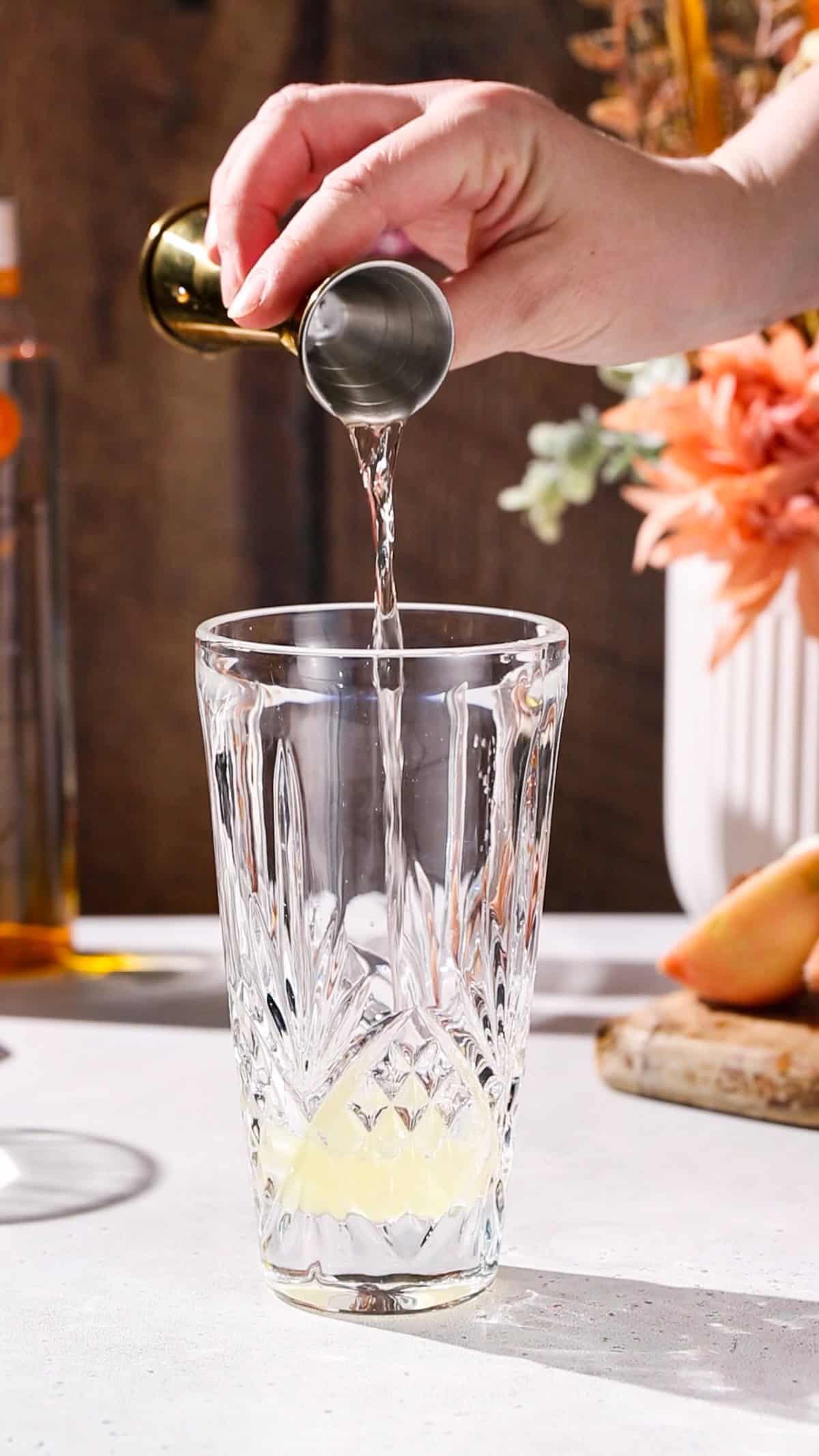 Hand using a jigger to add peach schnapps to a cocktail shaker.