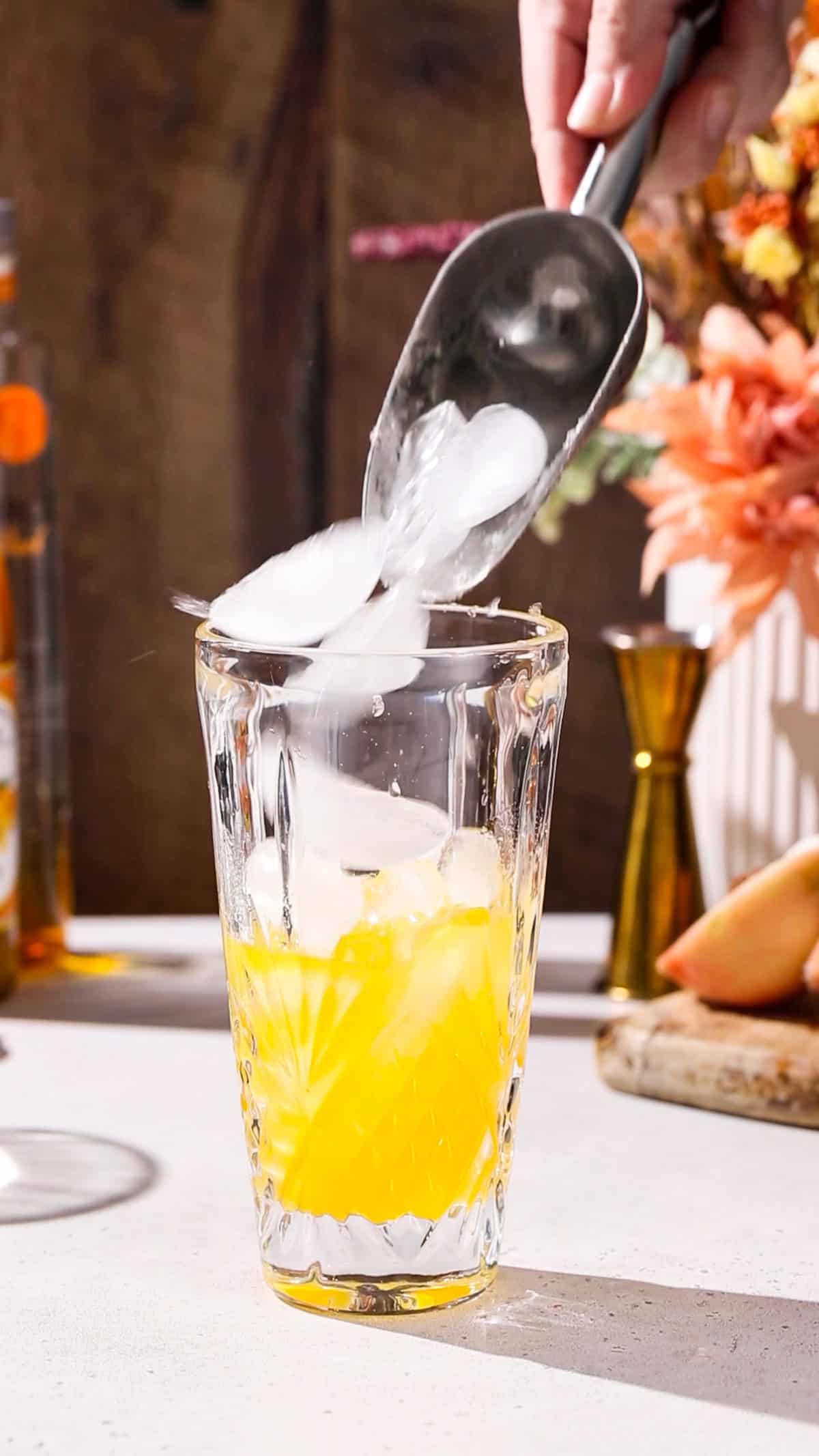 Hand using an ice scoop to add ice to a cocktail shaker.