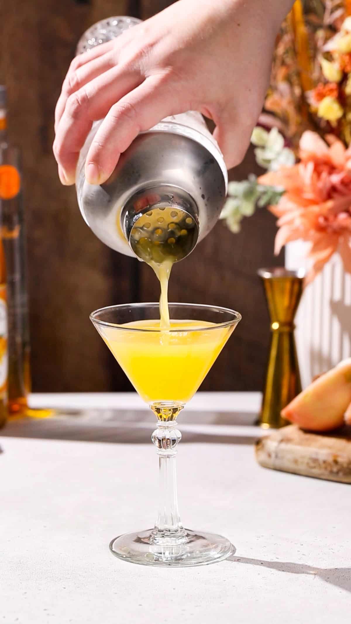 Hand straining a cocktail into a martini glass.