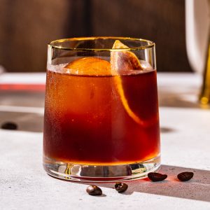 Side view of a Coffee Negroni with coffee beans scattered on the counter around it.