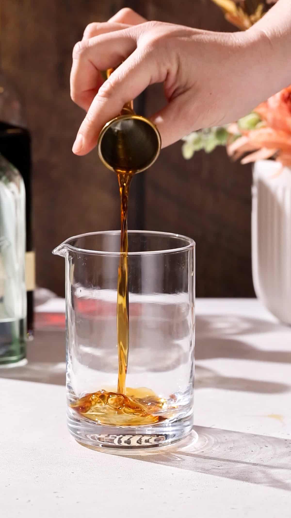 Hand pouring vermouth into a cocktail mixing glass.