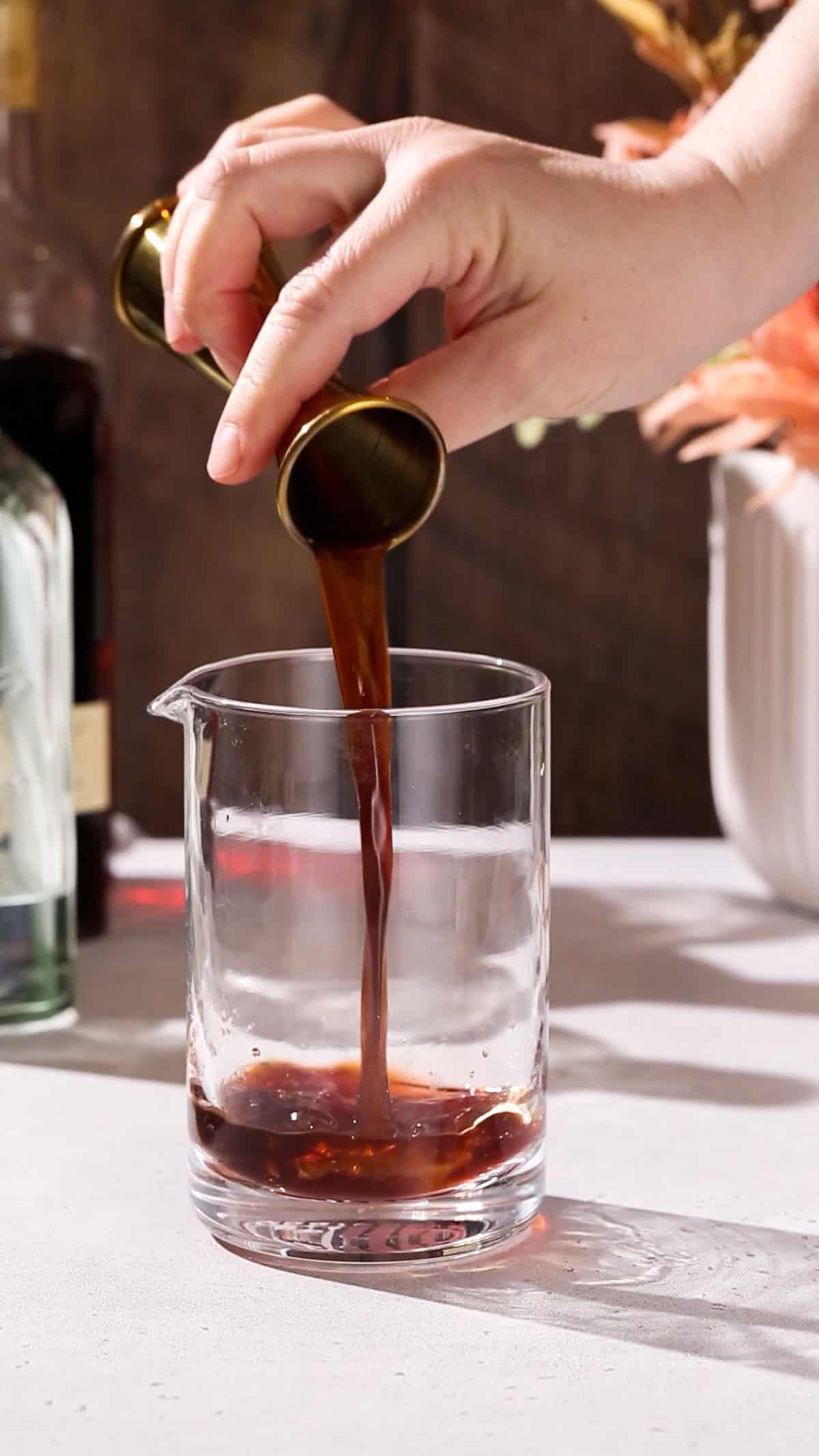 Hand pouring coffee liqueur into a mixing glass.