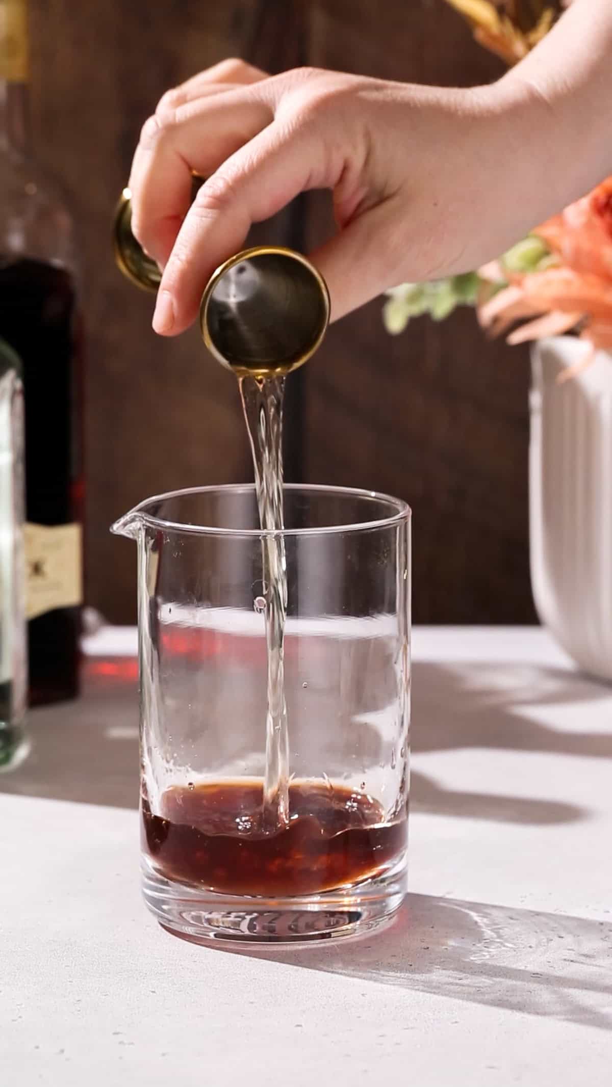 Hand pouring gin into a mixing glass.