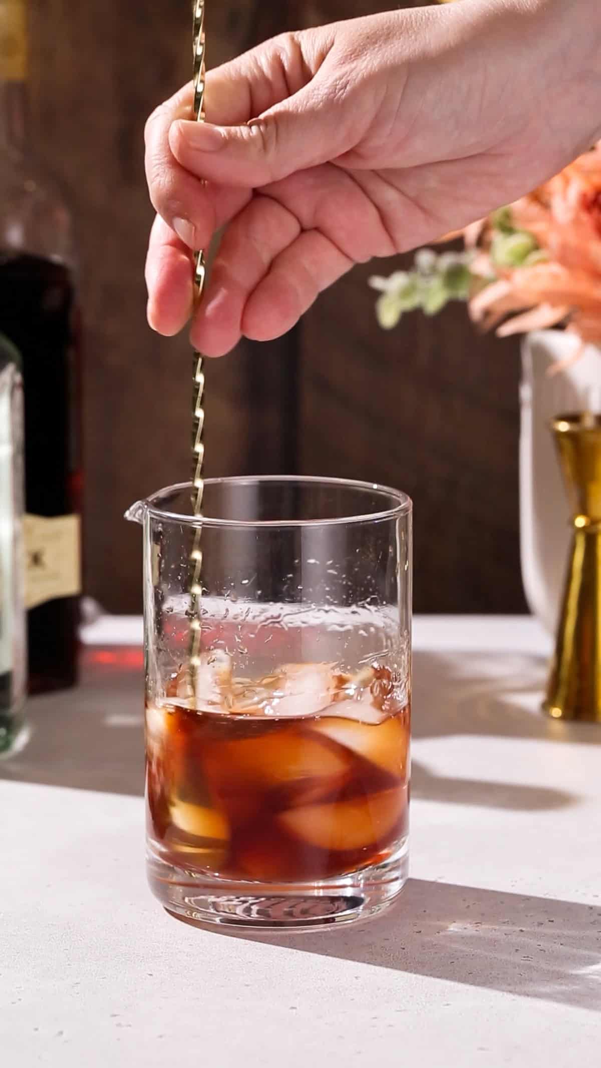 Hand stirring a cocktail in a mixing glass.