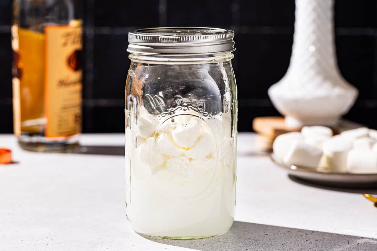 Side view of a jar of marshmallow infused vodka after sitting overnight. The marshmallows are not fully dissolved.