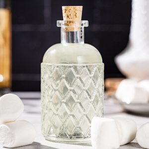 Side view of a glass bottle filled with a slightly cloudy liquid, marshmallow vodka. There are marshmallows all around the sides of the bottle.