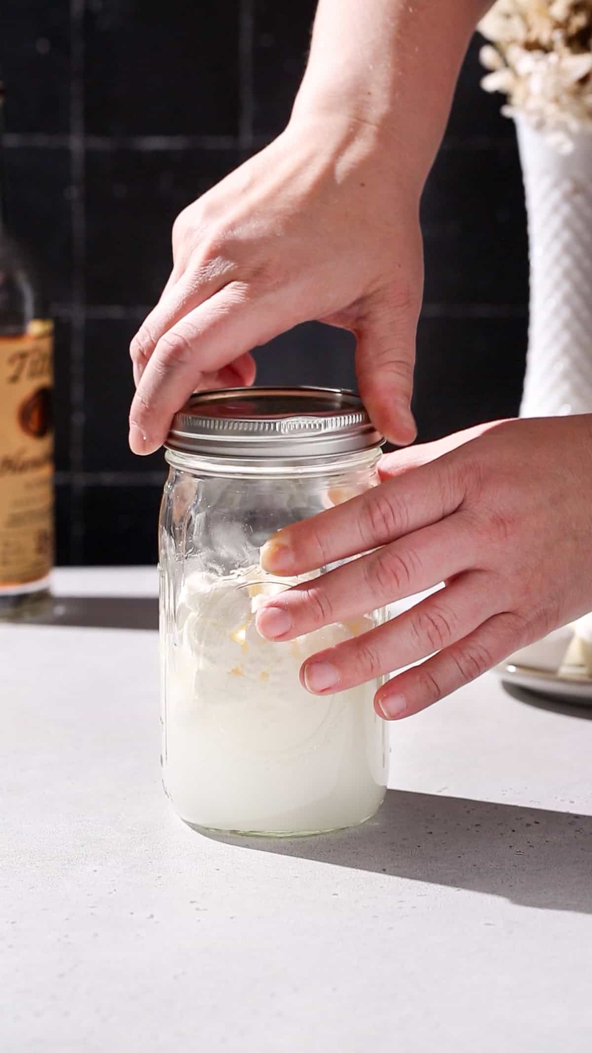 Hand closing the lid on a jar of marshmallows and vodka.