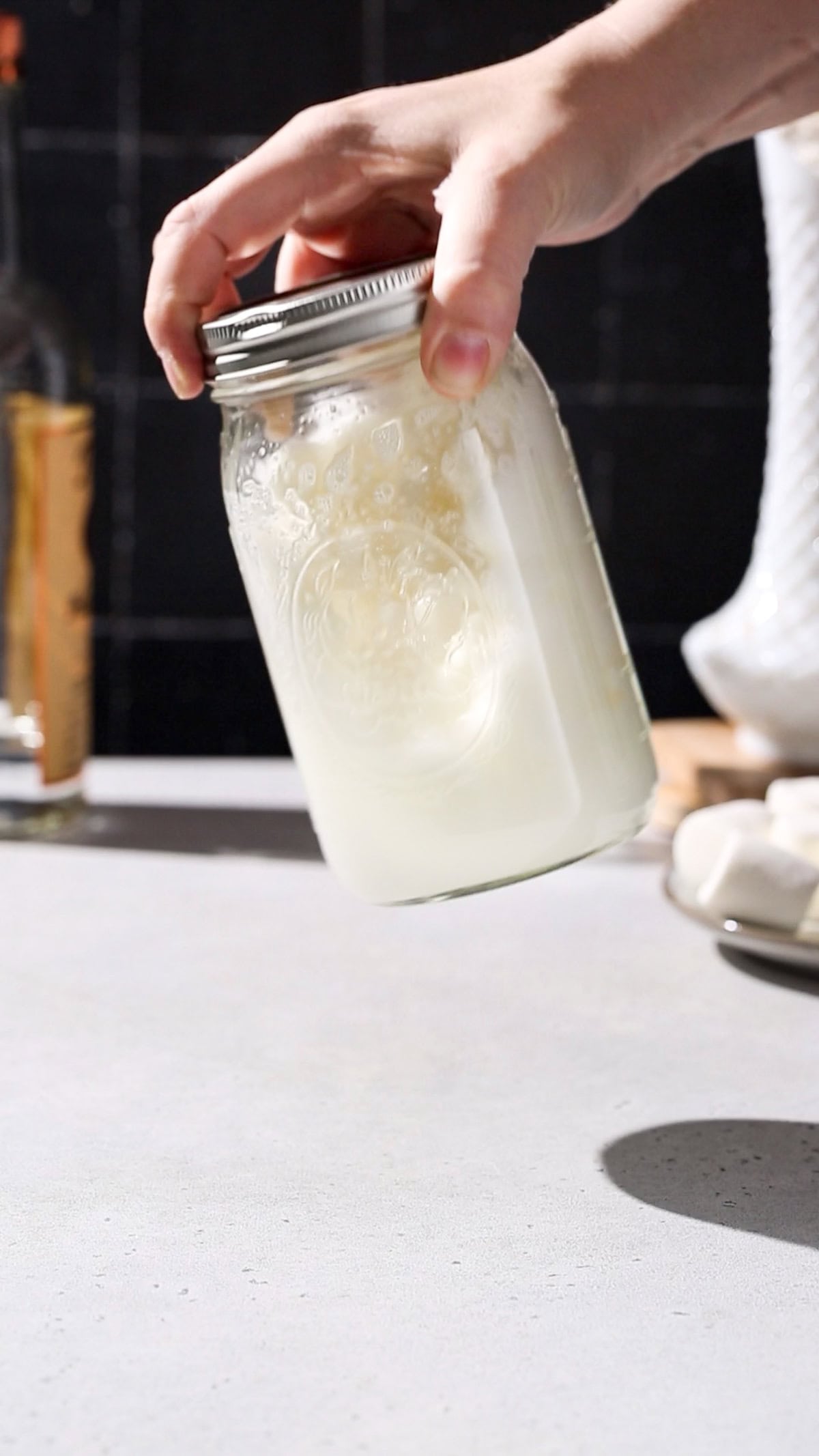 Hand shaking up a jar filled with marshmallows and vodka.