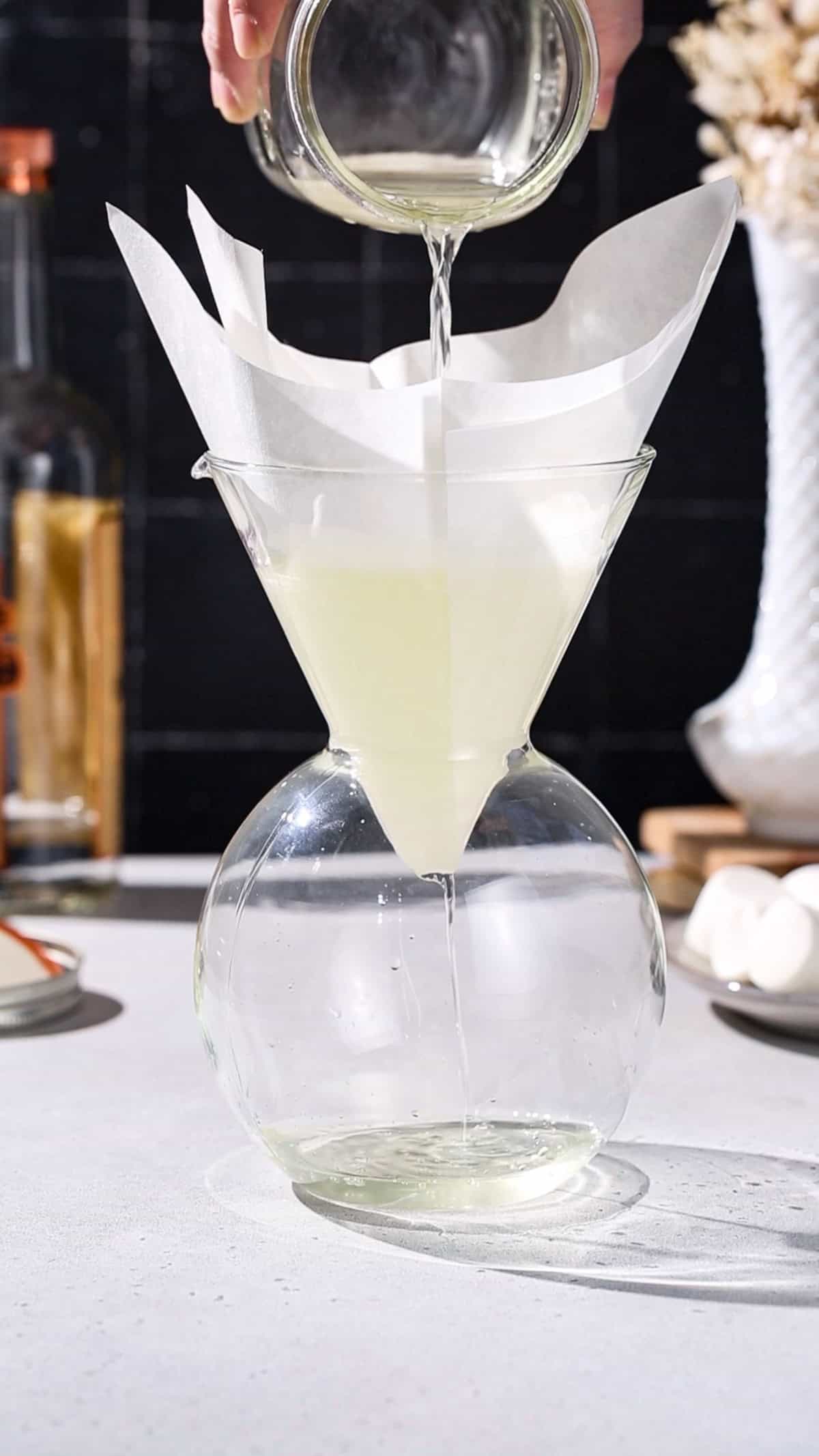 Hand pouring infused vodka through a coffee filter.