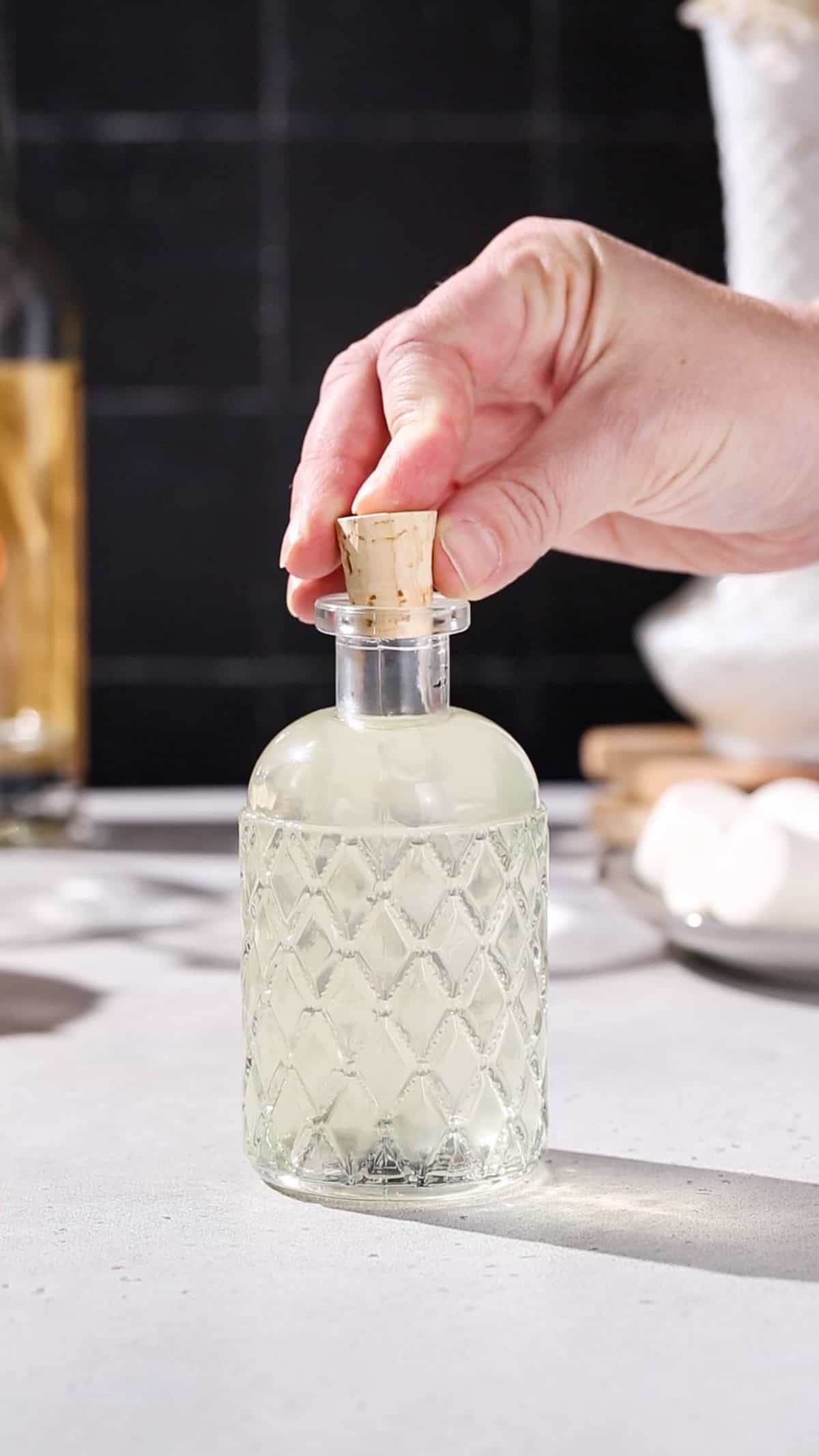 Hand adding a cork to a bottle of homemade marshmallow vodka.