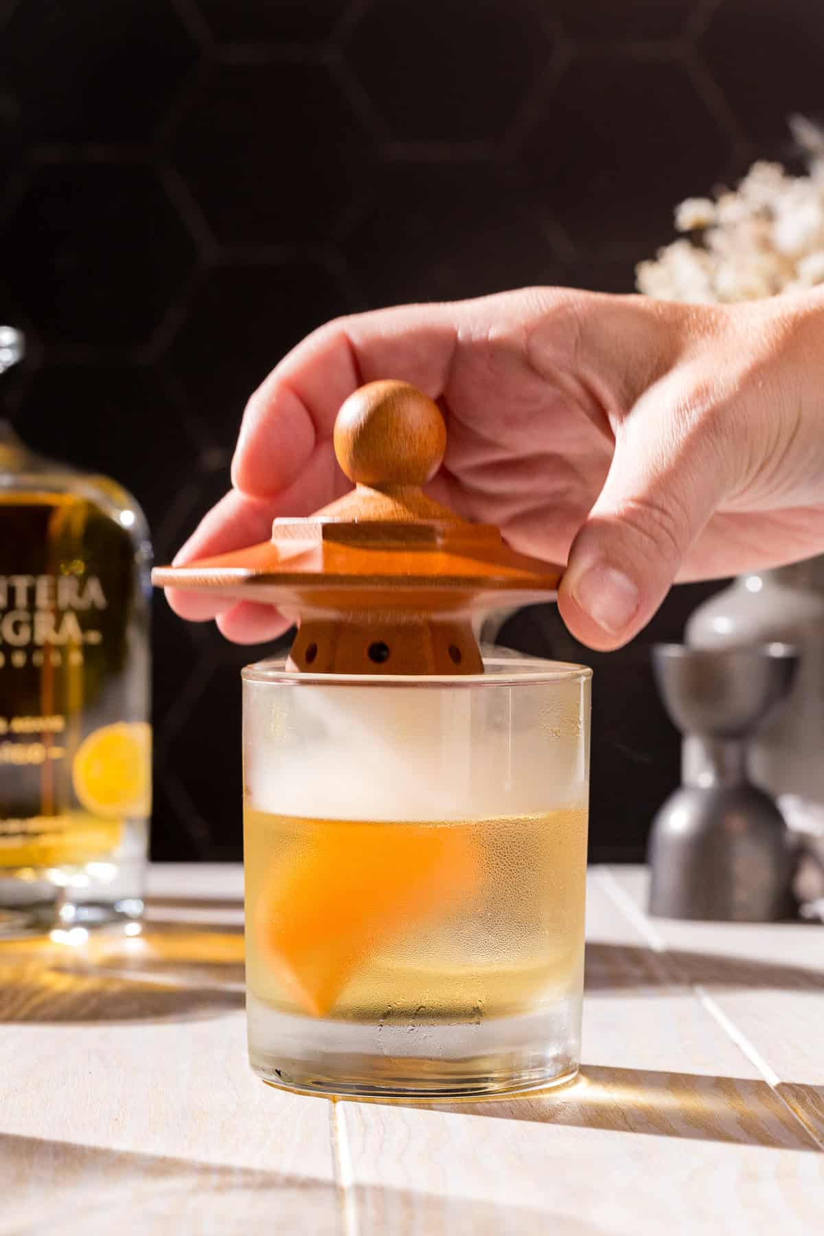 Hand removing a cocktail smoker from the top of an old fashioned glass. There is smoke still in the glass.