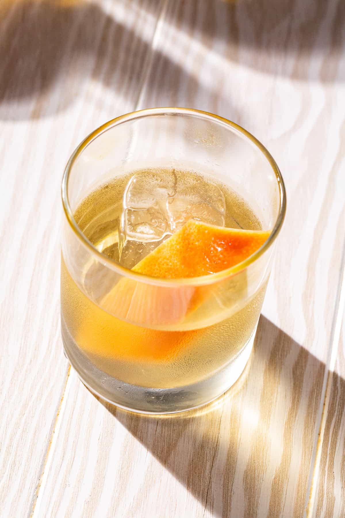 Top view of a Smoked Añejo Old Fashioned cocktail on a whitewashed wooden countertop.