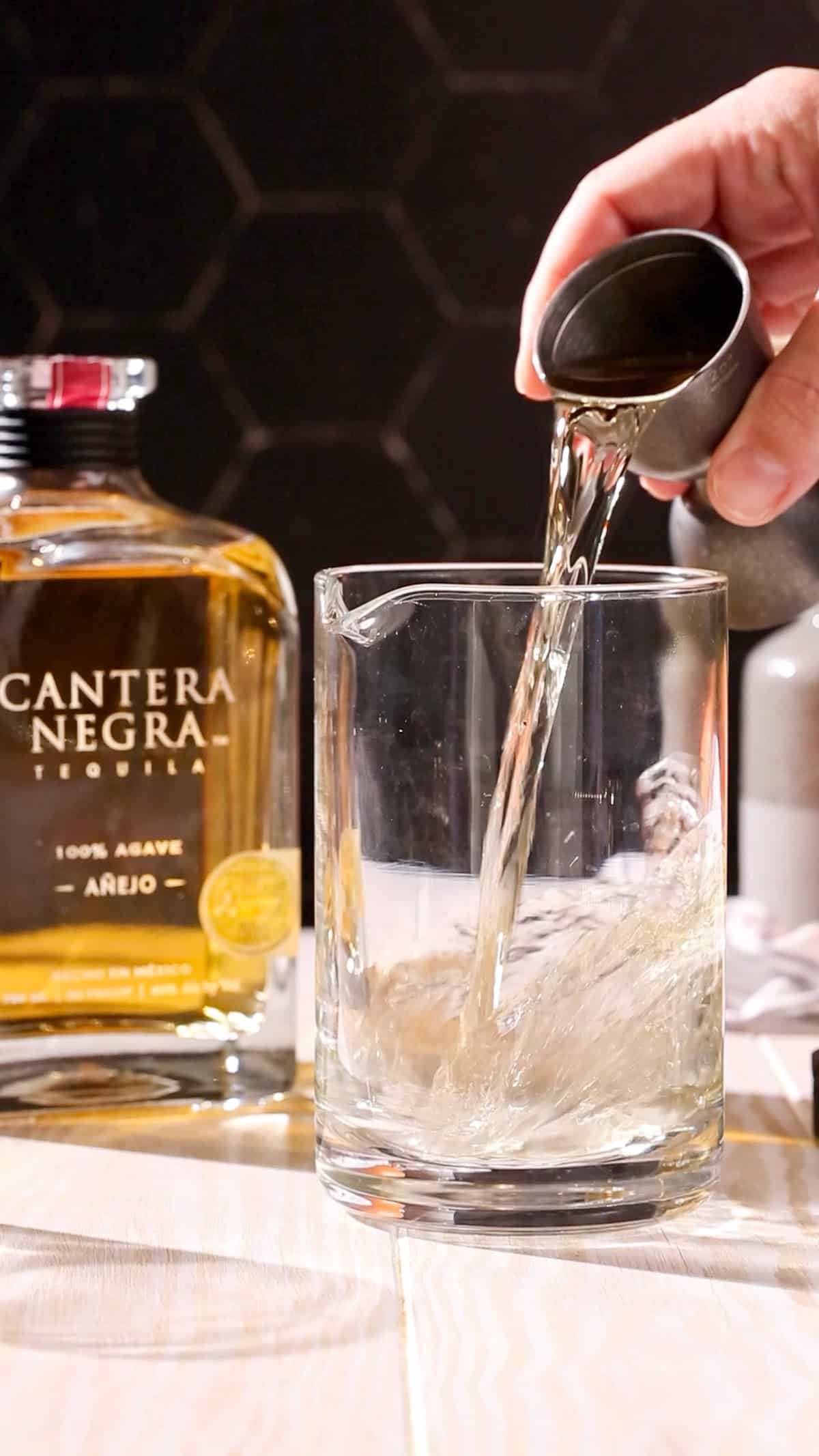 Hand adding anejo tequila to a cocktail mixing glass.