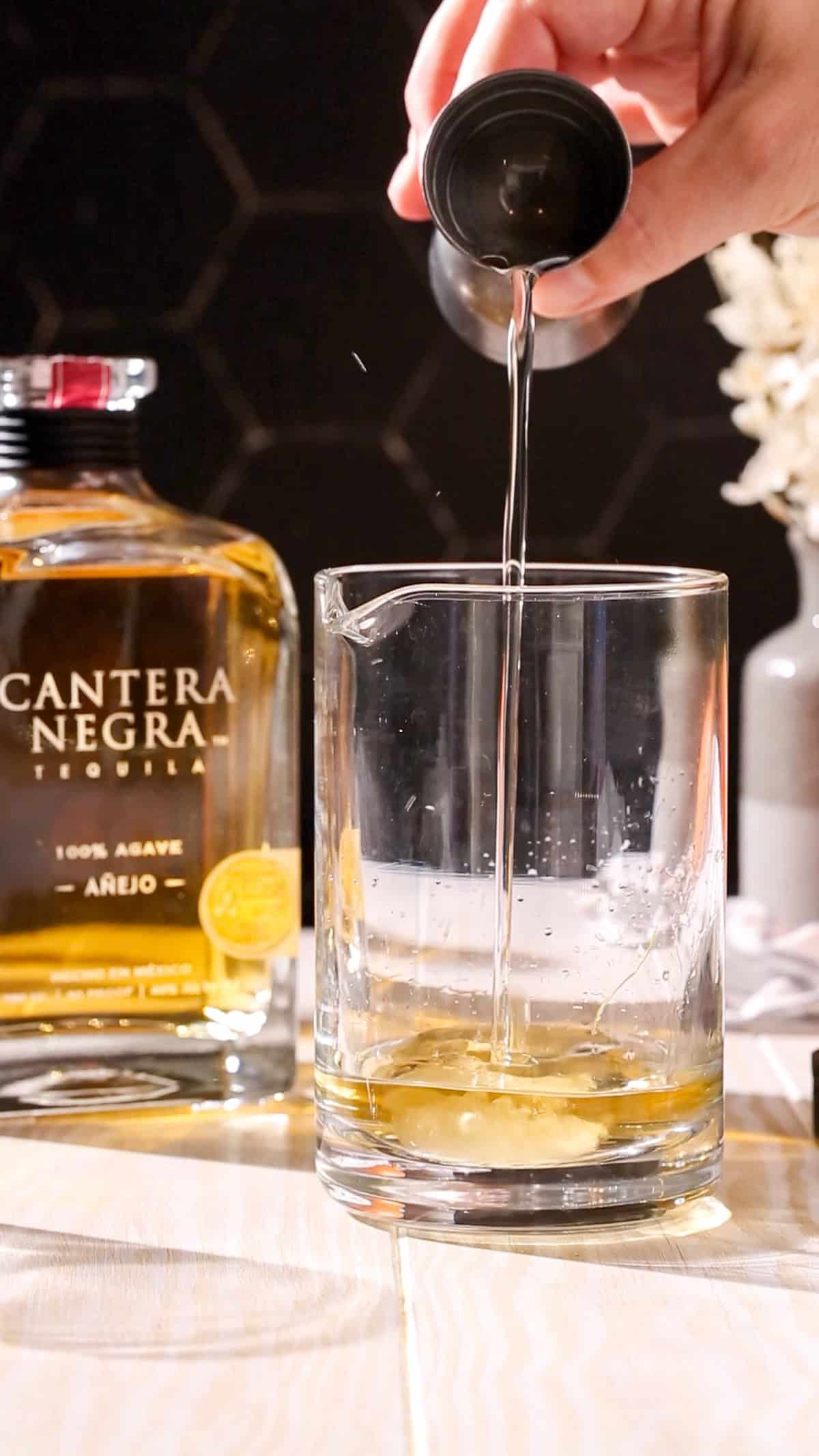 Hand adding simple syrup to a cocktail mixing glass.