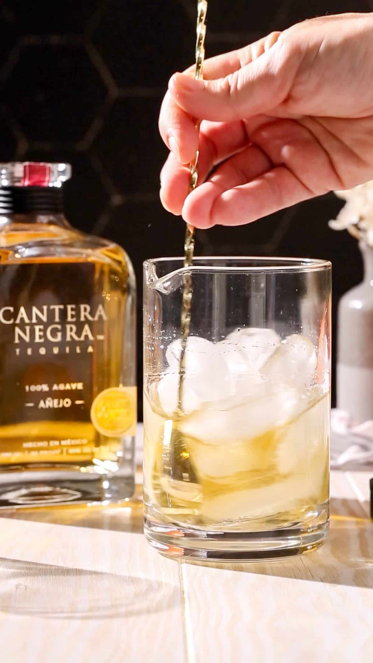 Hand using a bar spoon to stir a cocktail.