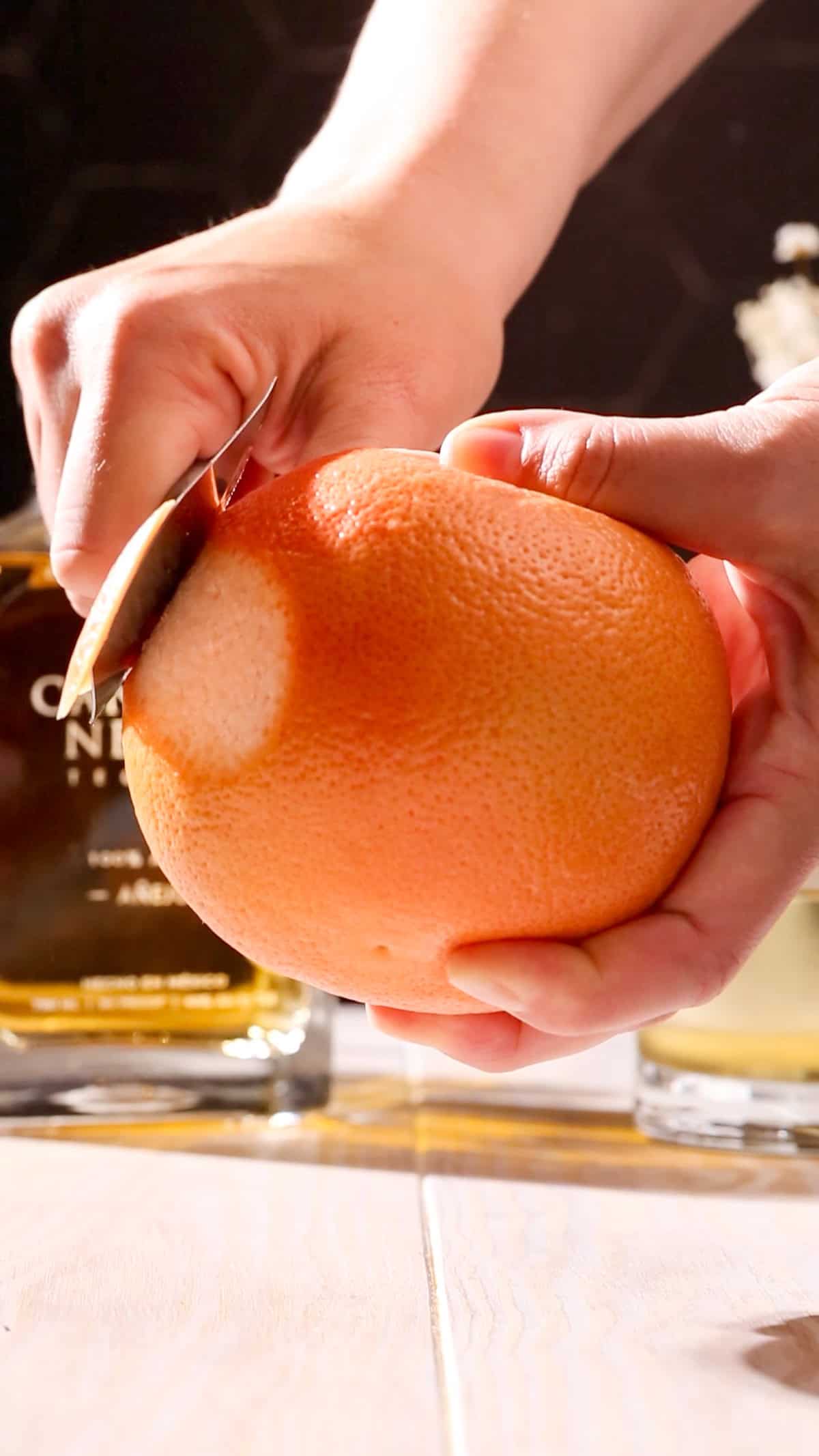 Hand using a vegetable peeler to peel a piece of grapefruit rind.