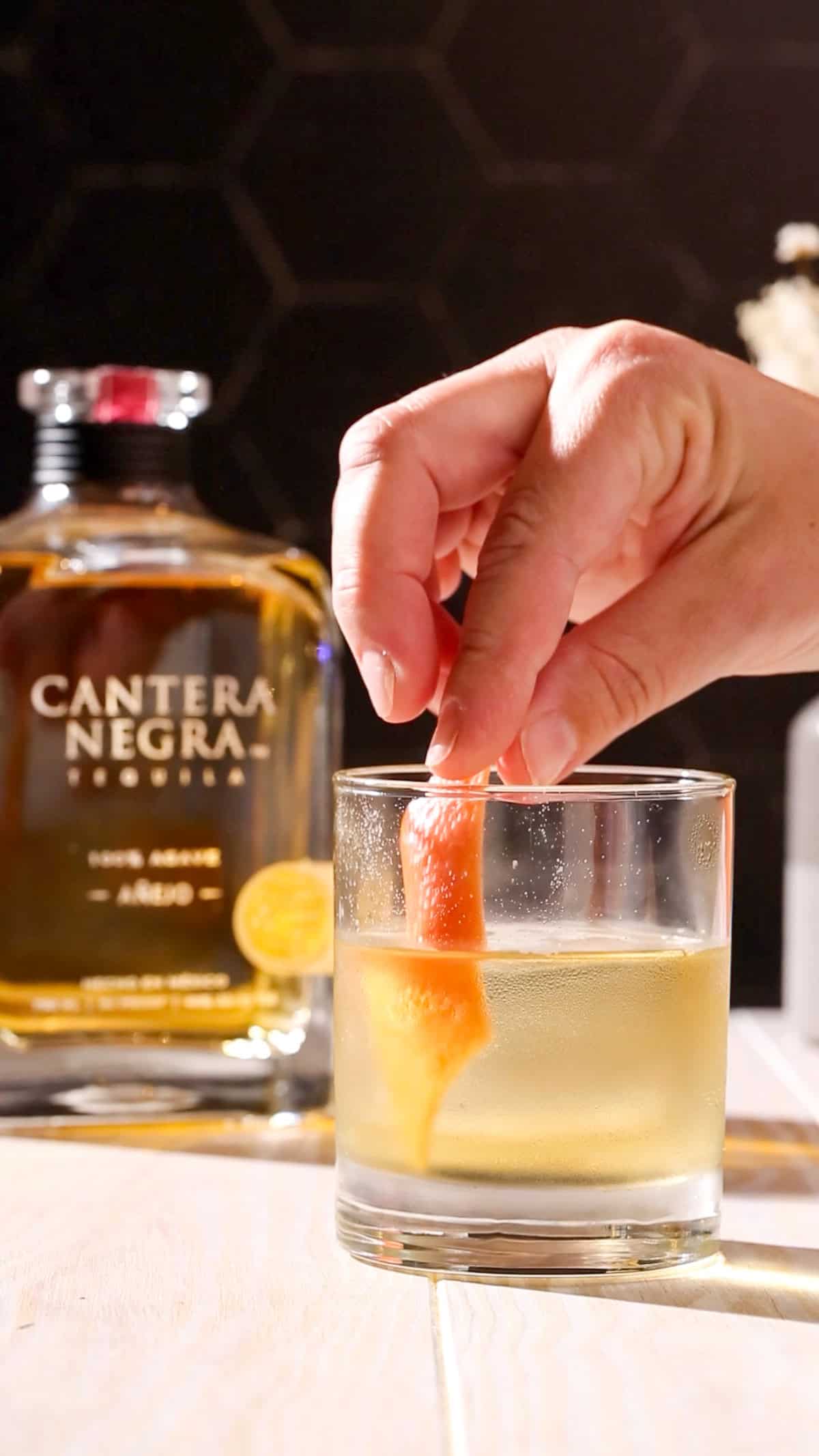 Hand adding a grapefruit peel to an anejo old fashioned.