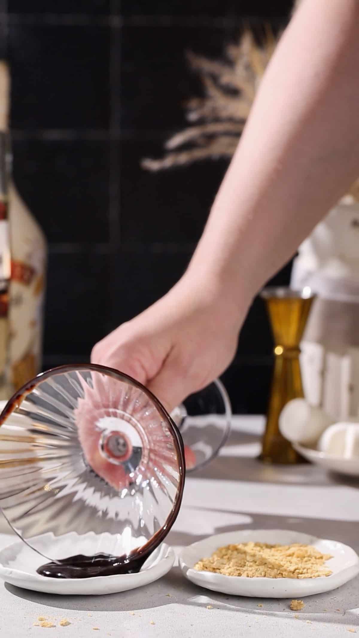 Hand dipping the rim of a martini glass into chocolate syrup.