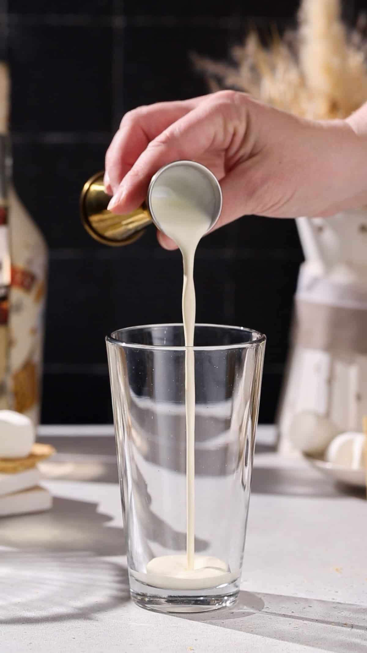 Hand pouring cream into a cocktail shaker.