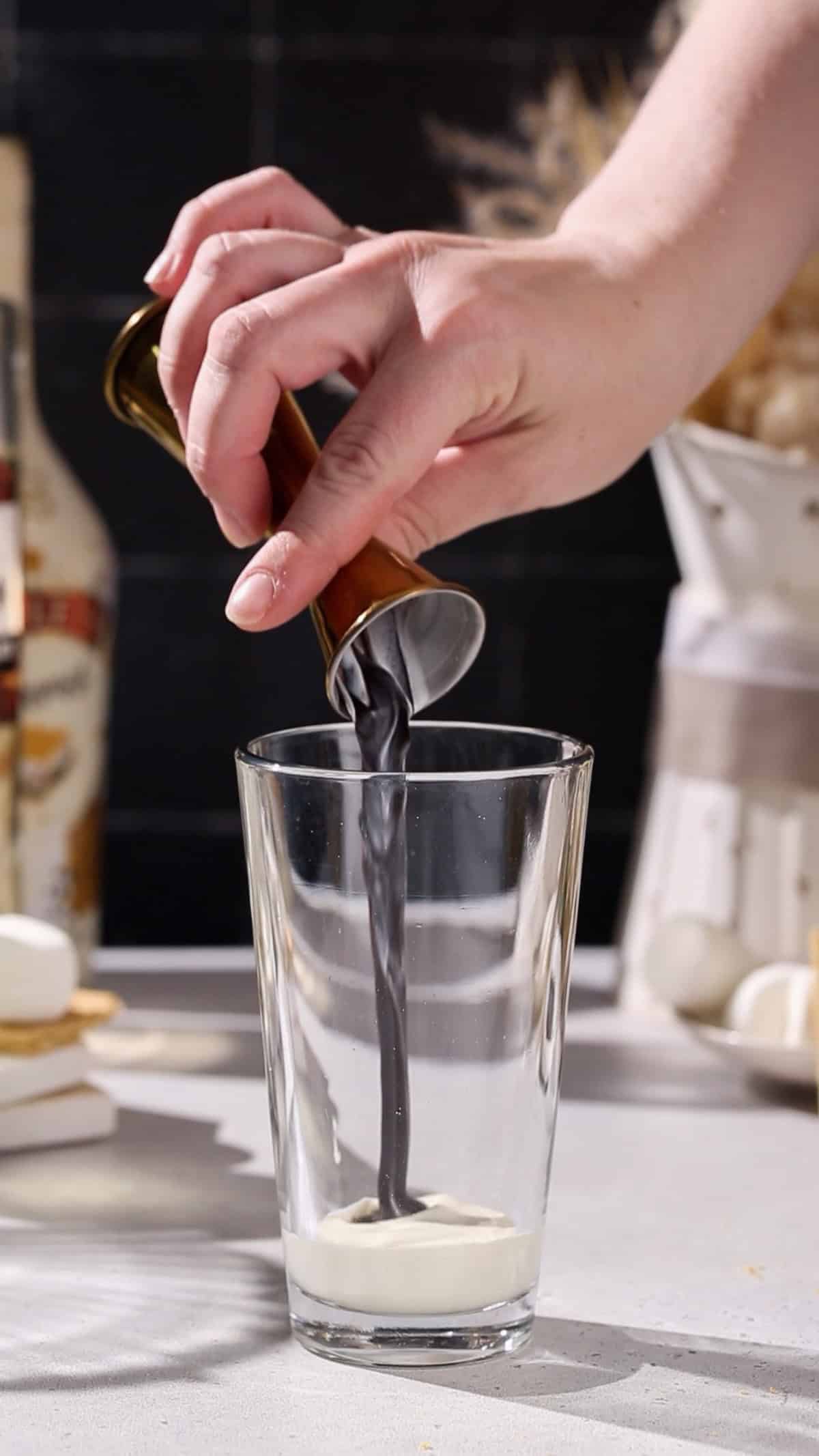 Hand pouring chocolate syrup into a cocktail shaker.