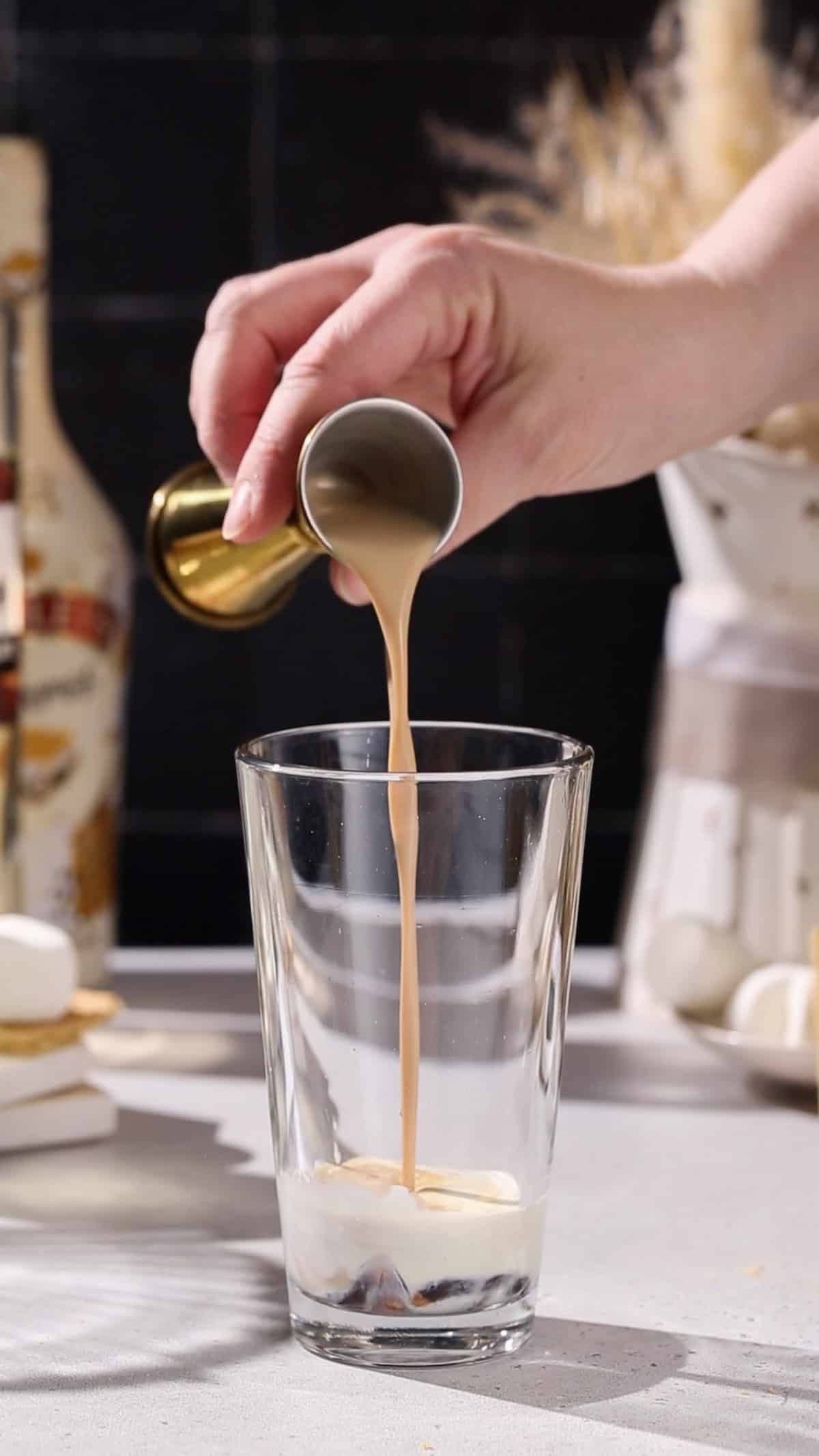 Hand pouring baileys liqueur into a cocktail shaker.