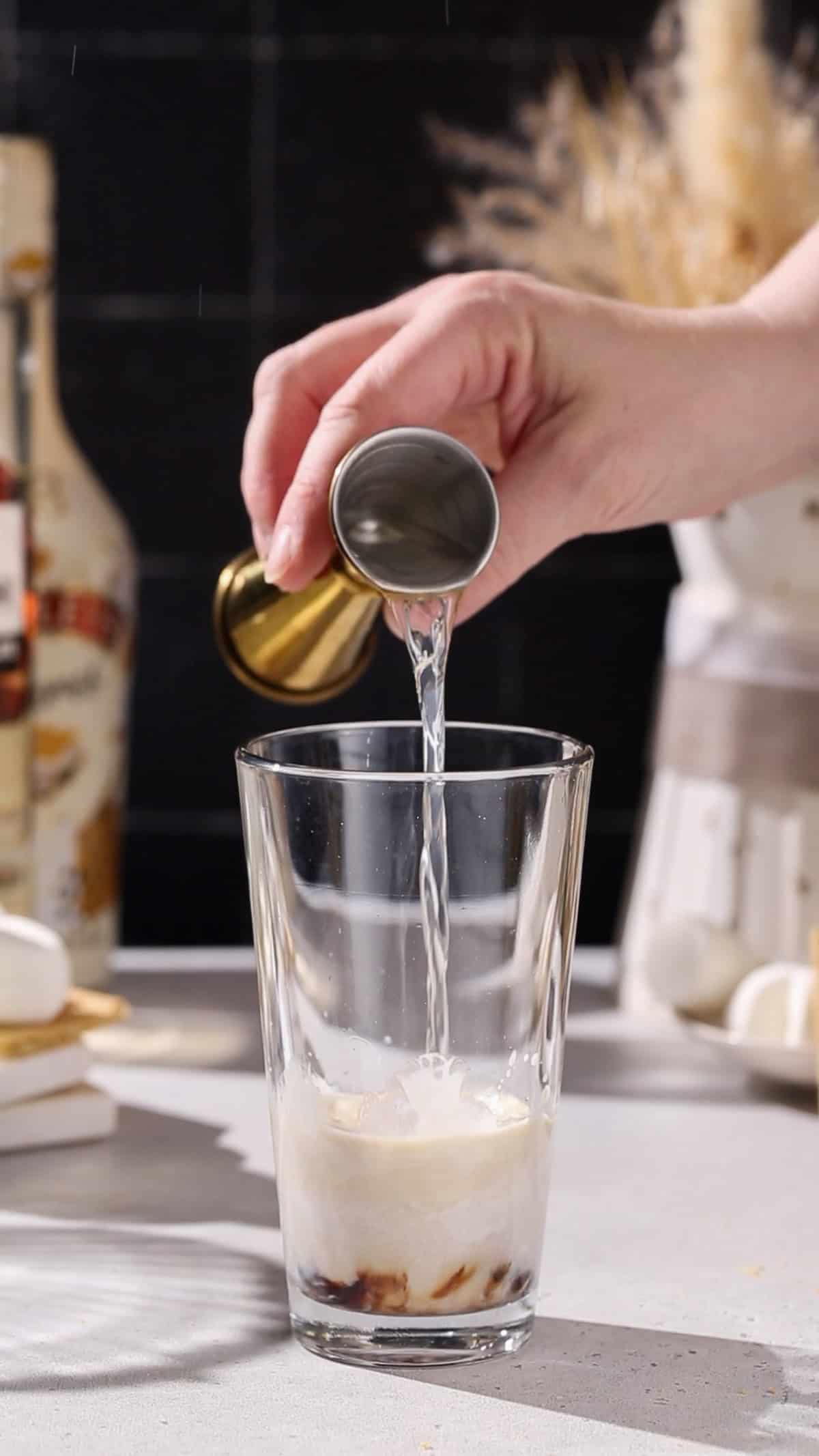 Hand pouring vodka into a cocktail shaker.